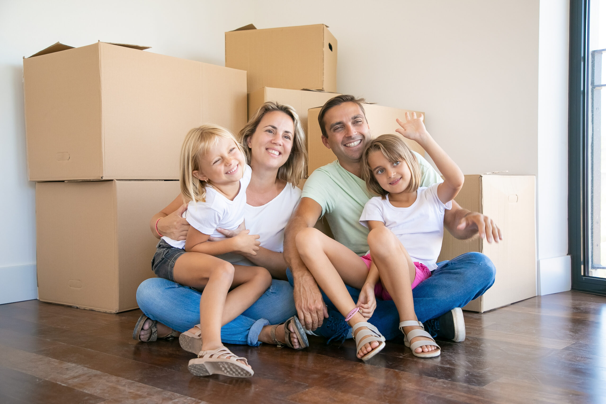 Smiling family with kids sitting on floor near cardboard boxes
